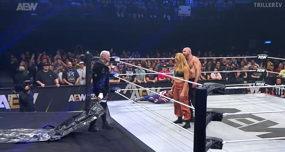 Darby Allin approaching the Death Riders, half his face painted like a skull, trailing a black body bag behind him.