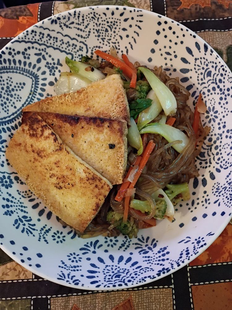 A bowl of glass noodles stir fried with veggies and topped with tofu slices.