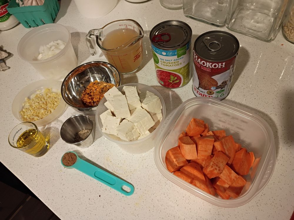 Chopped onion, minced garlic and ginger, olive oil, spices, vegetable broth, tofu, crushed tomatoes, coconut milk, and sweet potato.