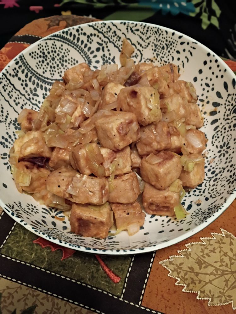 A bowl of tofu that was marinated, floured, and stir-fried, with leeks and onions.