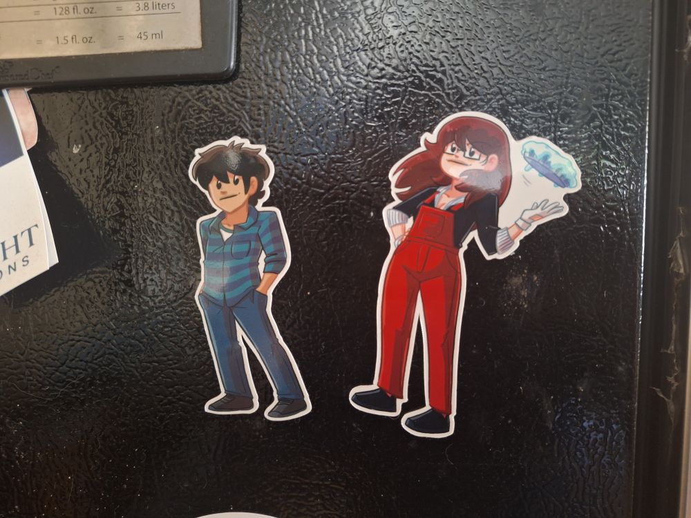 Two magnetic characters: a black-haired guy and a brown-haired girl with glasses. He included a third one that I think is the character who looks the most like Helen from my webcomic Narbonic.