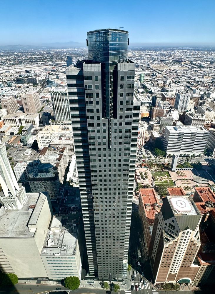 Grey postmodern office tower with football shaped crown. Downtown Los Angeles is below and beyond