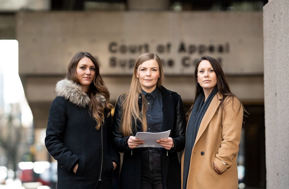 Emma Gilchrist, Amber Bracken and Carol Linnitt stand with serious expressions in front of a court building. Amber holds a document in her hands.