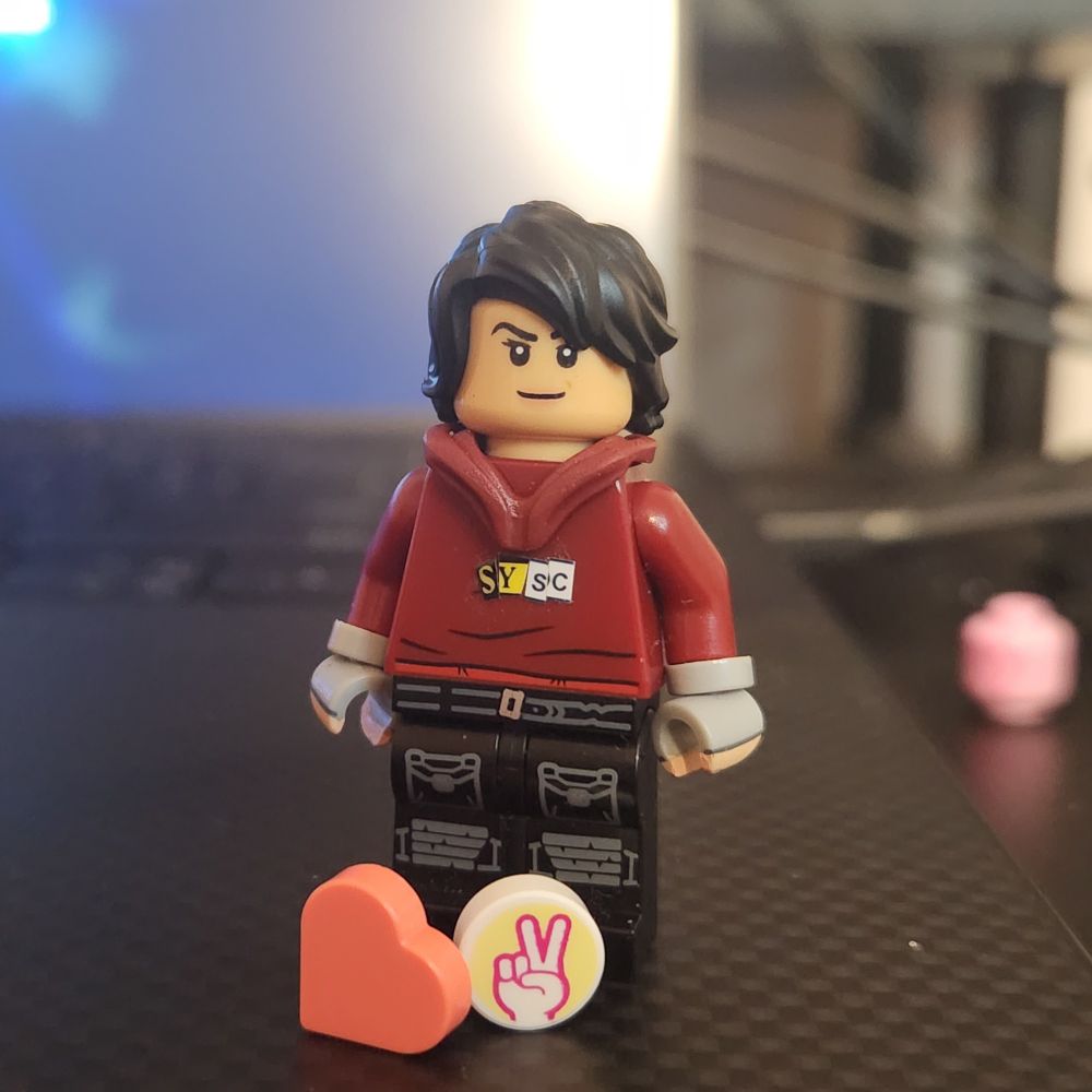 me as a lego minifigure in a maroon hoodie reading "SYSC" with a heart and peace sign on tiles at her feet 🫶✌️