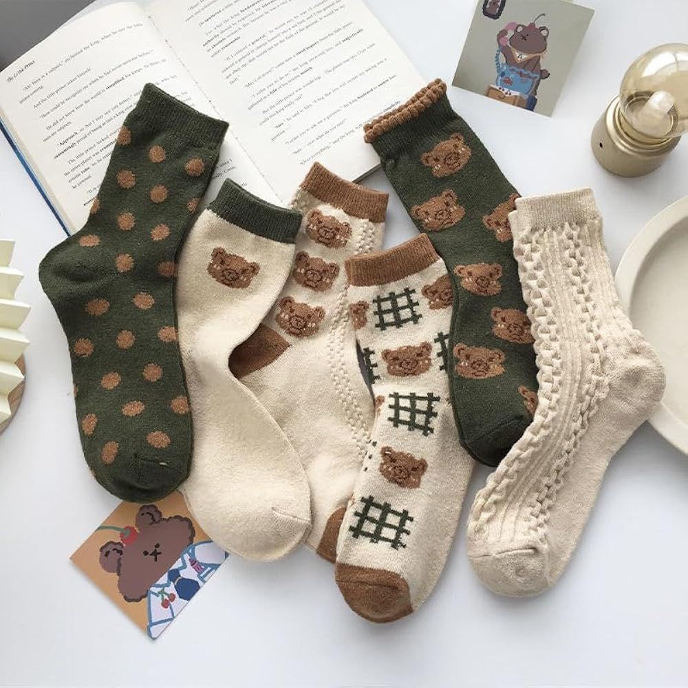 5 pairs of socks, from left to right: a green pair with brown dots. A white pair with a green strip on the top and a bear, a white pair with brown accents and bears, a white pair with brown accents, hashtags, and bears, a green pair with bears, and a white frilly pair. 
