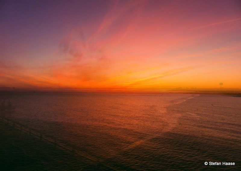 A colorful sunset casts brilliant shades of red and gold across the ocean's surface, reflecting the day's end. / Ein farbenfroher Sonnenuntergang taucht die Meeresoberfläche in leuchtende Rot- und Goldtöne und spiegelt das Ende des Tages wider.