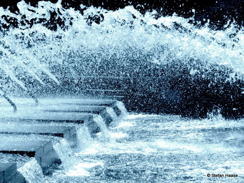 Man sieht mehrere Wasserfontänen, aus denen Wasser spritzt. Sozusagen ist das Wasser in Bewegung./ You can see several water fountains from which water is spraying. The water is in motion, so to speak.
