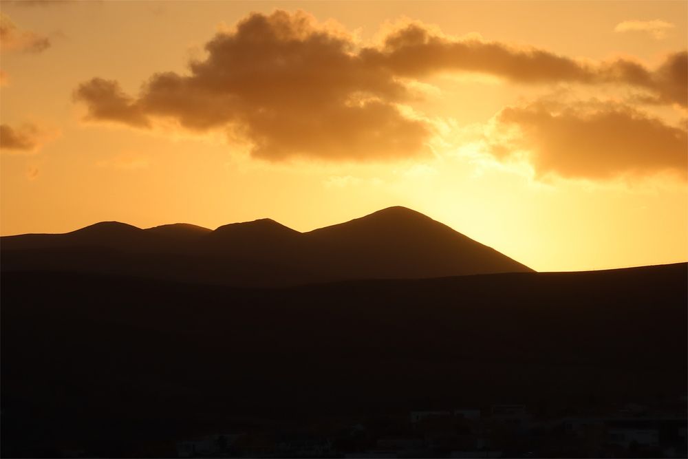A setting sun casting a mountain in silhouette 