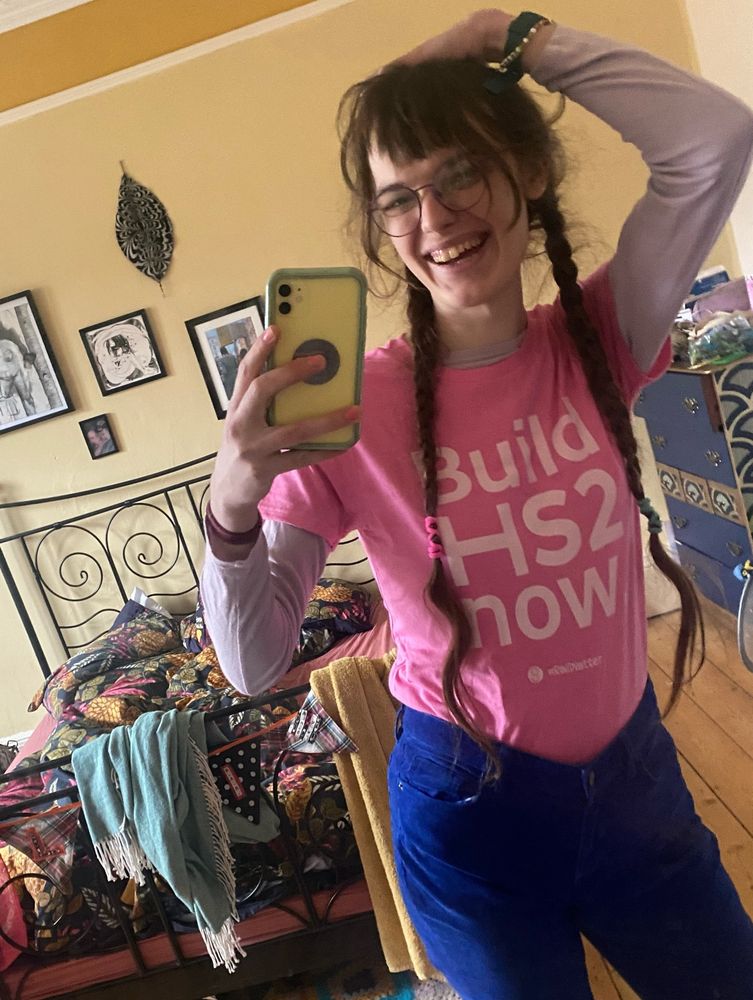 mirror selfie of white trans woman  wearing a pink t-shirt with the words "Build HS2 Now"