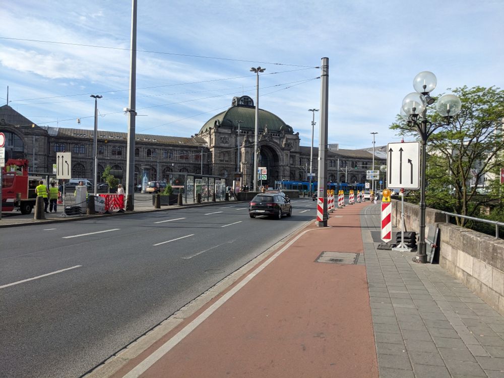 Auf dem Gehweg abgestellte Schilder und Banken für den PkW-Verkehr behindern Menschen auf dem Fahrrad und zu Fuß.