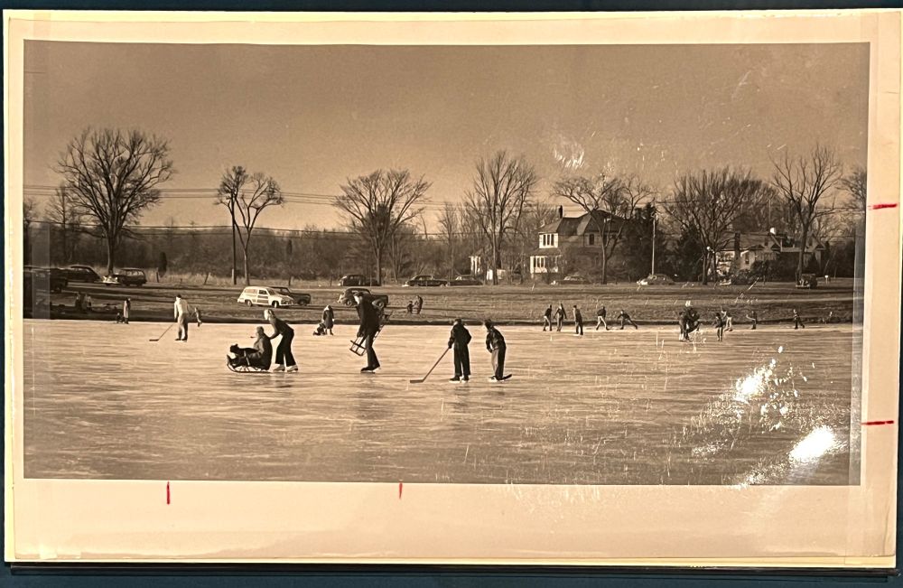 black and white photograph of skaters playing hockey on a frozen lake