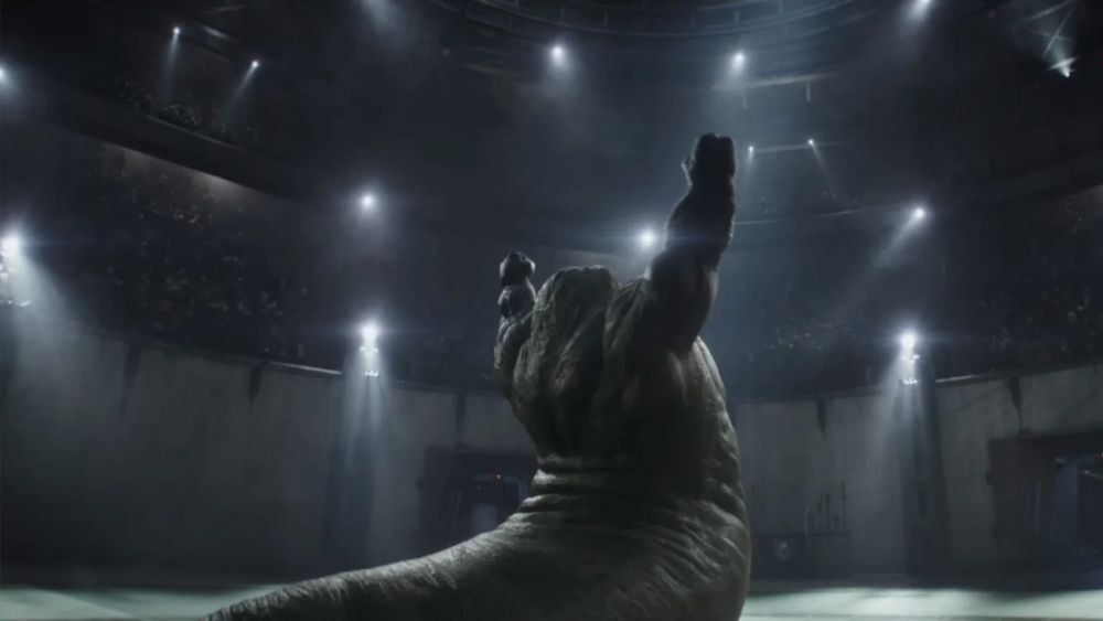 Rotta the hutt with muscly arms raised in a wrestling arena. From the Mandalorian and Grogu film trailer. 