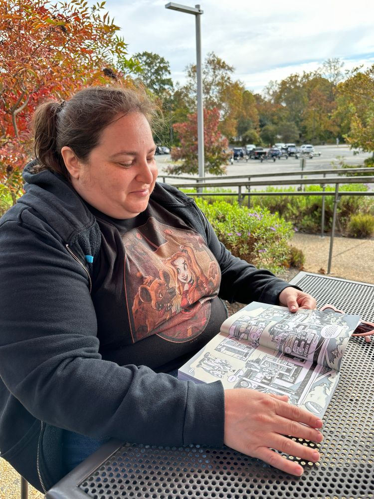 Kira is reading a comic while hanging out at the Occoquan Park. 