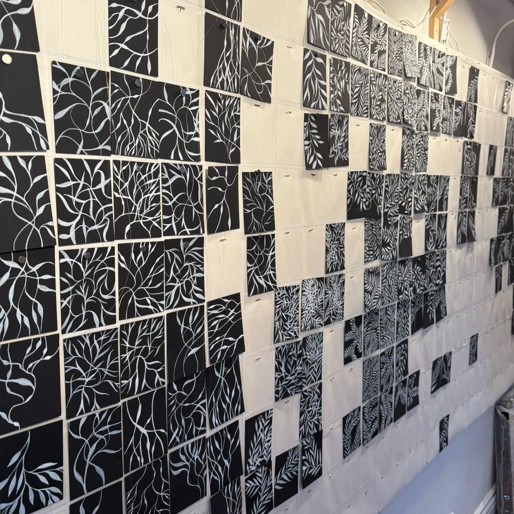 Incomplete grid of small rectangles of black paper with white organic plant patterns painted on them