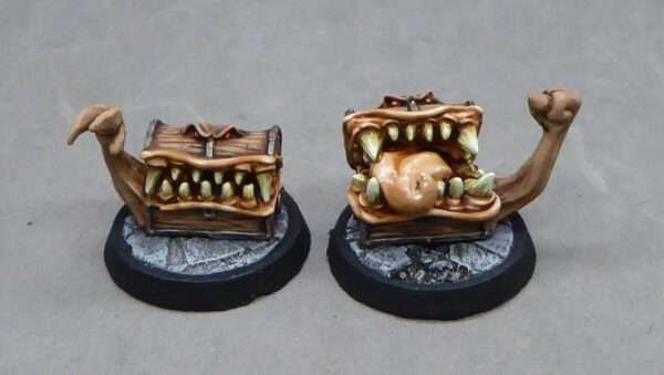 Two tabletop-scaled treasure chest mimics, one reaching out with a claw, the other offering up a jelly-like fist. Both are full of teeth and tongue and eyes.