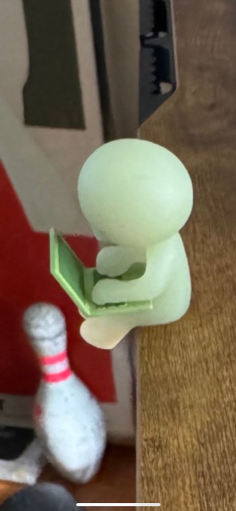 A closeup from John’s image, focusing on a little, greenish figurine of a person sitting with a laptop. 