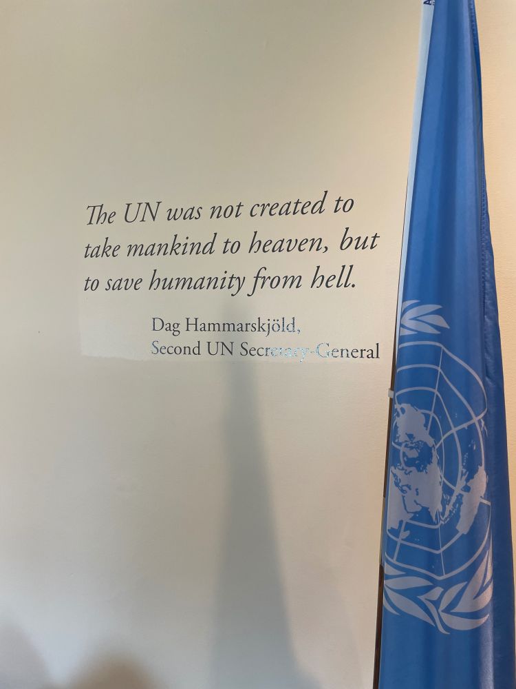 Quote “the UN was not created to take mankind to heaven, but to save humanity from hell.” Dag Hammarskjöld, second UN secretary general. On wall of UN building with a blue UN flag. 