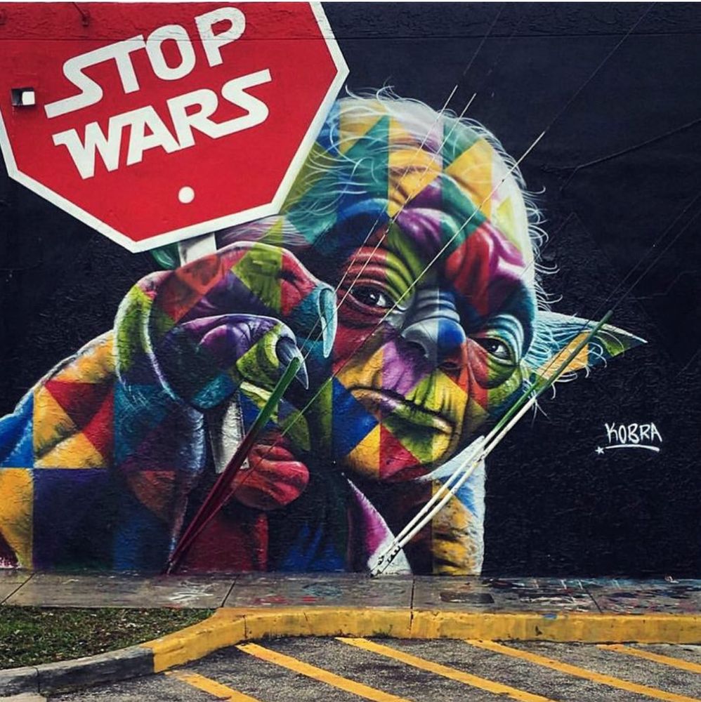 Graffiti art on an exterior wall with a multicolored Yoda from Star Wars holding a red stop sign that says Stop Wars