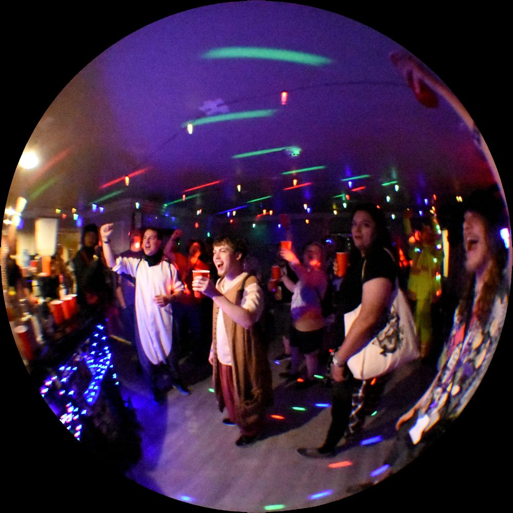 A fisheye image of the audience response to the last hurrah at Las Vegas Furcon 2025. The guests raise their cups into the air cheering on just as the con are about to end (just before 2 am monday morning)

Here is an excerpt about this scene from my essay on furrycon room parties: 

I managed to capture some of the celebration at the very end of the convention. These events are happening mere hours before the 11am checkout time on Monday Morning. A quite literal last hurrah of the night, a celebration to the inevitable end of the convention and the transformations that have happened.

The intense atmosphere of this moment stands with me. There was such a strong sense of the end, something this is encroaching. In the furry fandom this is called post con depression, it is a distinctly sad feeling, a pit in one's stomach, that is accompanied at the end of a furry convention. It is the feeling that you want this to last forever and you are faced with the inevitability that it must end. I find it amazing and quite interesting that there was a lingering sense at that moment to keep going as long as possible. We collectively avoid the tasks that are to come, we avoid the fact that this entire party space needs to be returned to the state of being a hotel room in just a few hours.