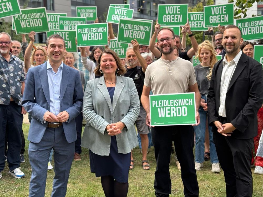 Outdoor group photo of Adrian, Ellie, Matt and Zack with large number of activists holding up bilingual Vote Green boards.