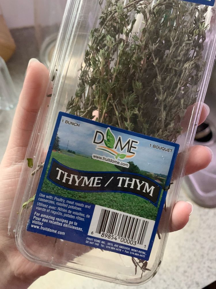 Ren's hand holding up a grocery store package of thyme, with a bilingual label that says "thyme/thym"