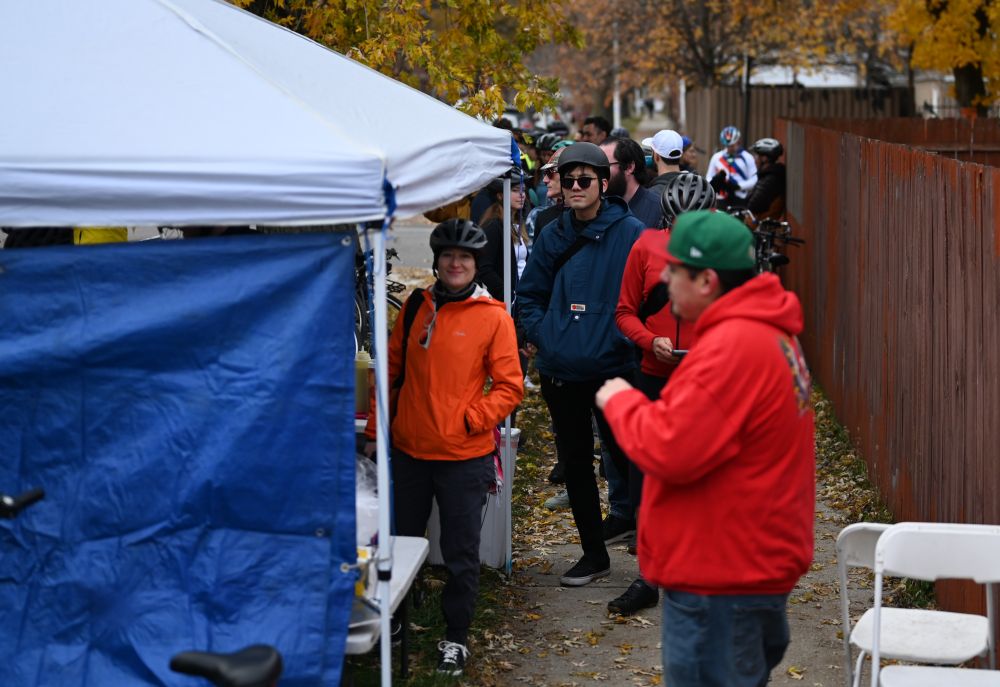 A line of dozens of people waiting behind a tent on an autumnal day