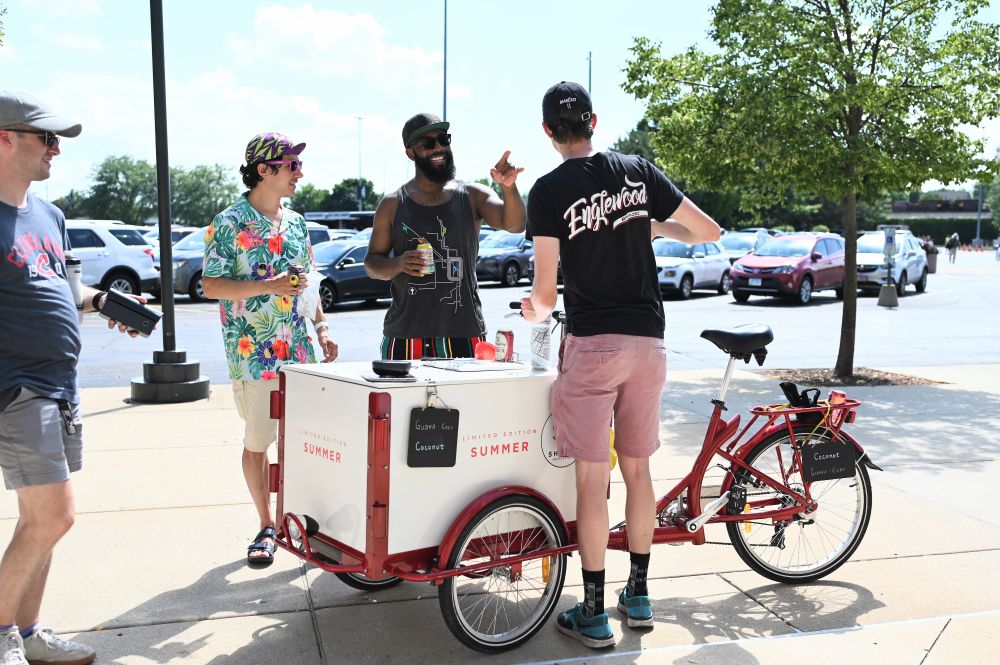 A red and white ice cream trike with Dietrich from Sherpa Pedal Cafe smiling wide behind it, with Daniel from Bike Sox to his left, and a man with his back to camera at the front