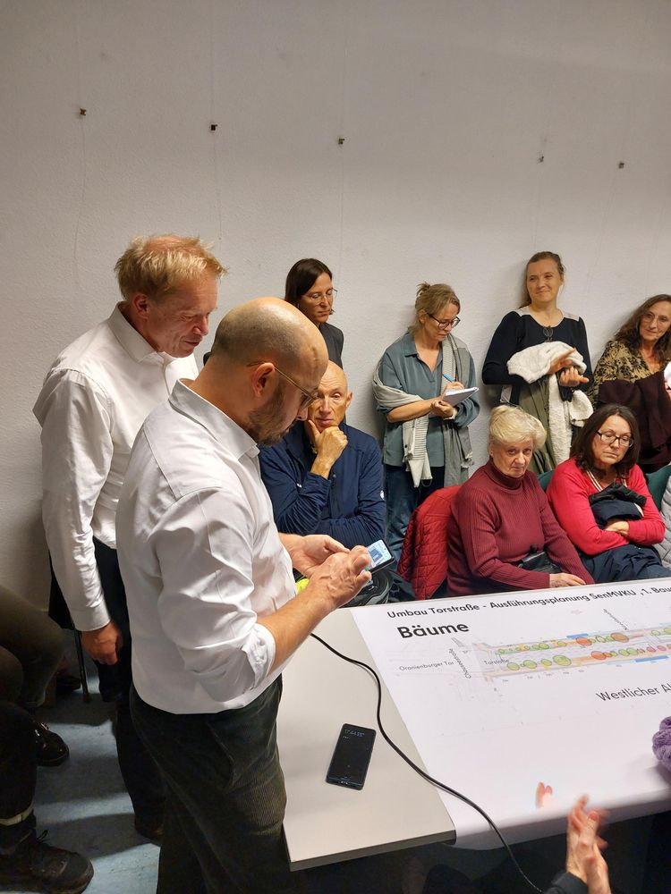 Viele Menschen stehen und sitzen in einem Raum. In der Mitte ein Tisch mit einer Karte der Torstraße.