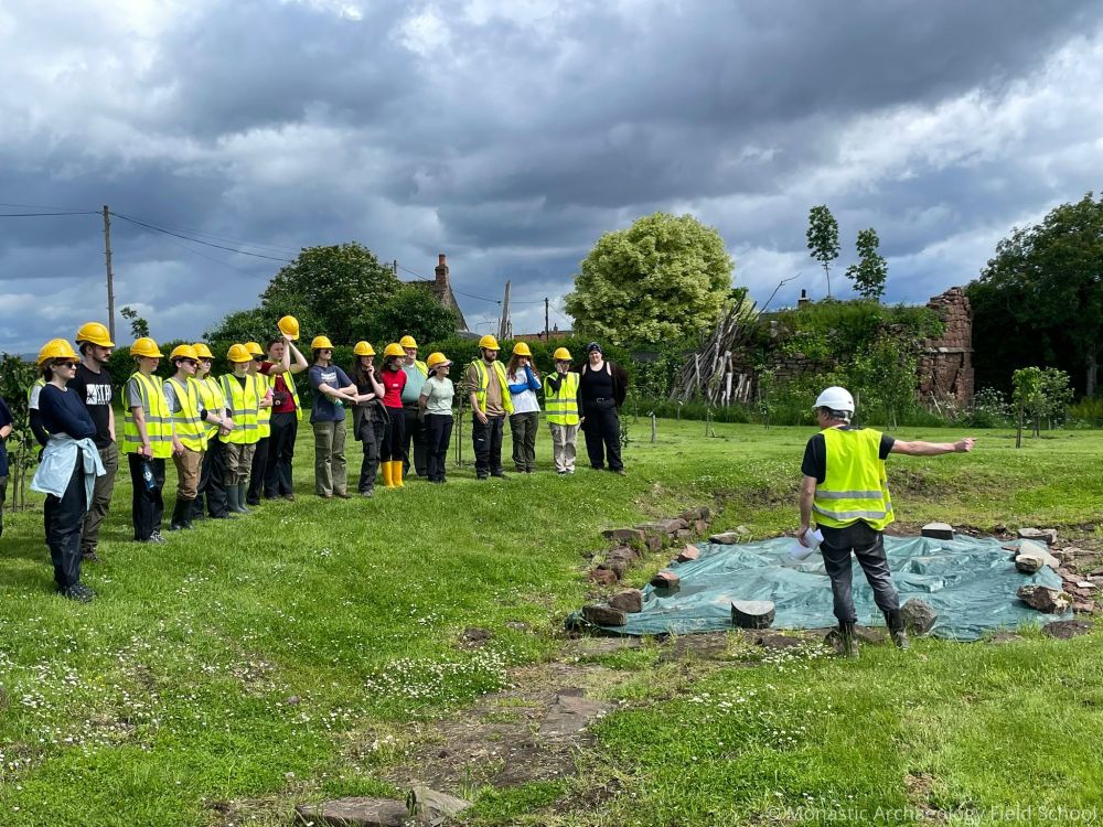 Several people in high-vis looking at a person talking near a trench 