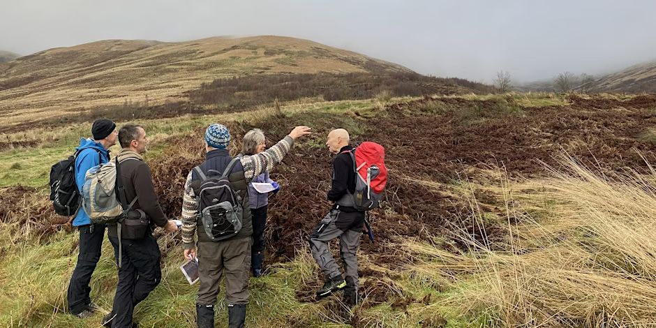 Group of people in outdoor clothes in a rural and hilly area - one person is pointing at something