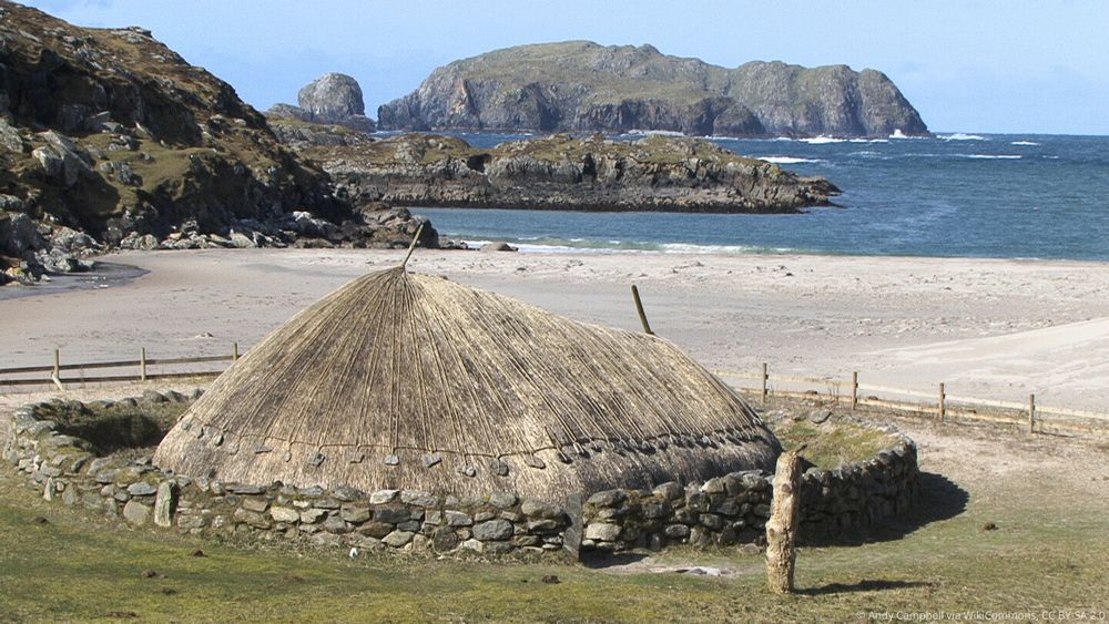 Photo of a reconstructed Iron Age house on a beach with islands in the sea in the distance