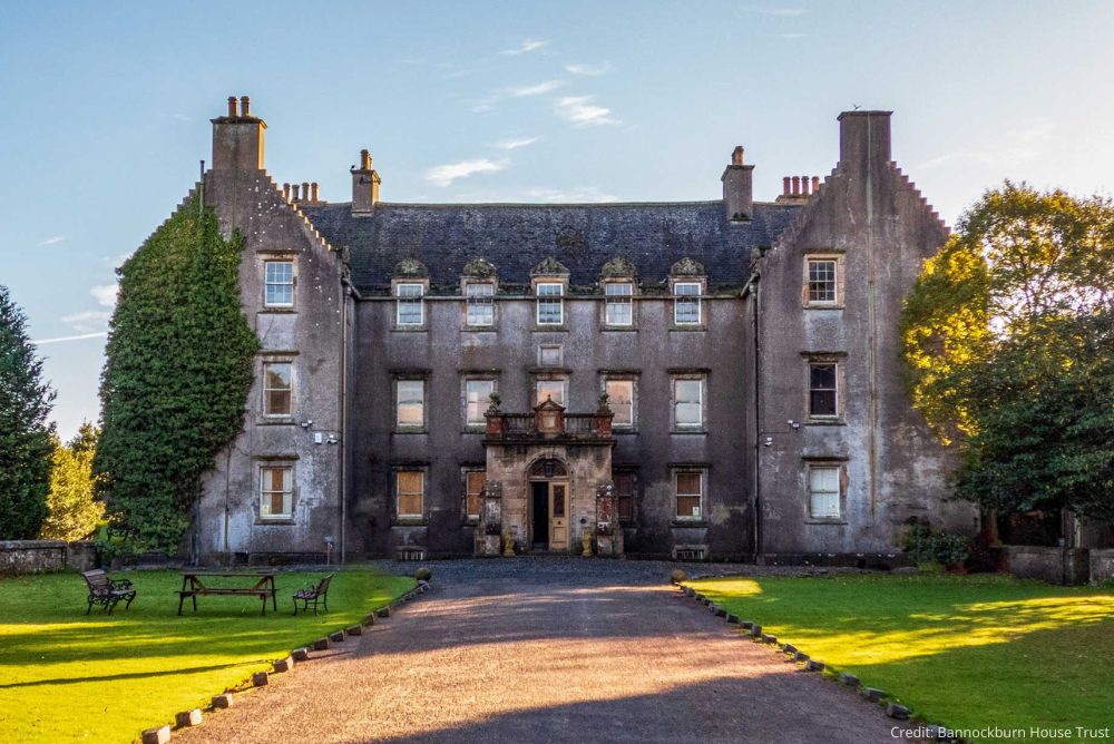 Photo of the front of a grand mansion with gravel driveway