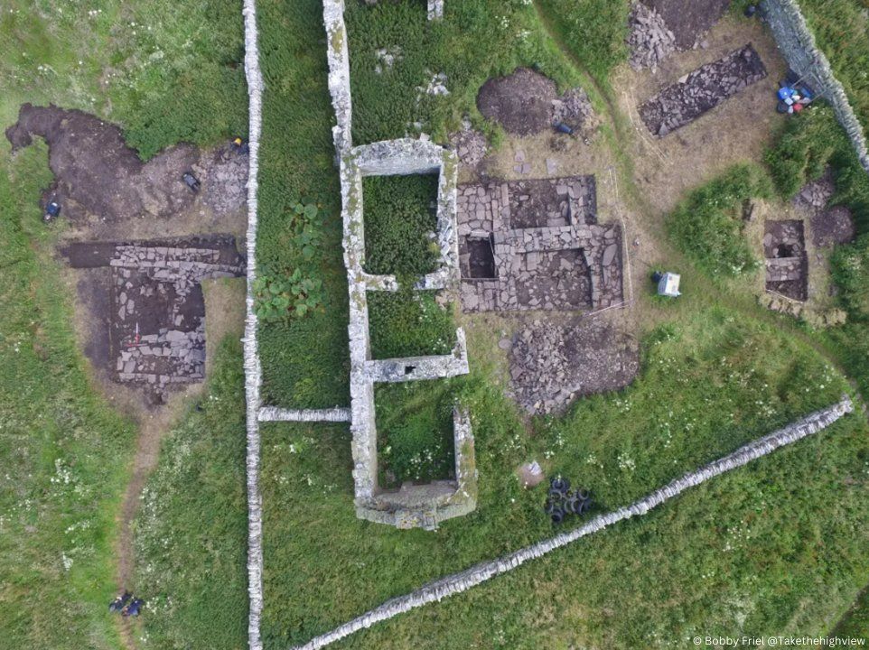 Aerial photo of the stone upstanding remains of a farm building, with several archaeological trenches revealed more underground stone foundations around it