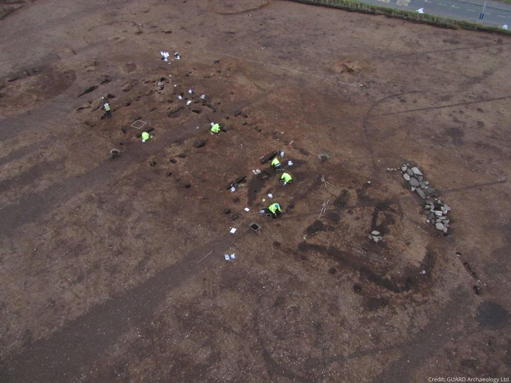 Aerial photo of archaeologists working in a field with the outlines of a Neolithic building visible in the earth