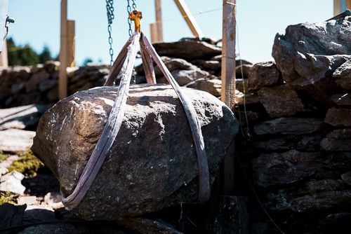 Ein grosser Stein wird mit einer Seilwinde für den Bau einer Trockenmauer angehoben.