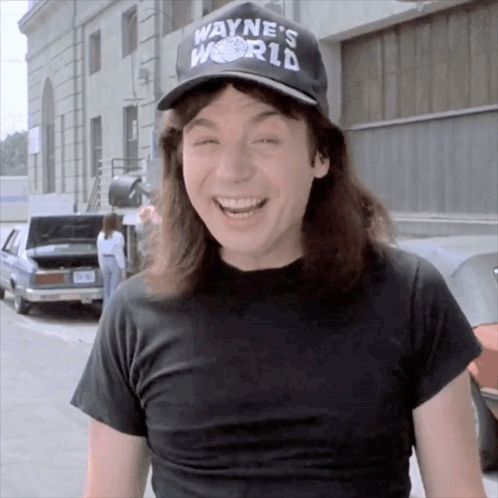 a man wearing a black shirt and a wayne 's world hat smiles