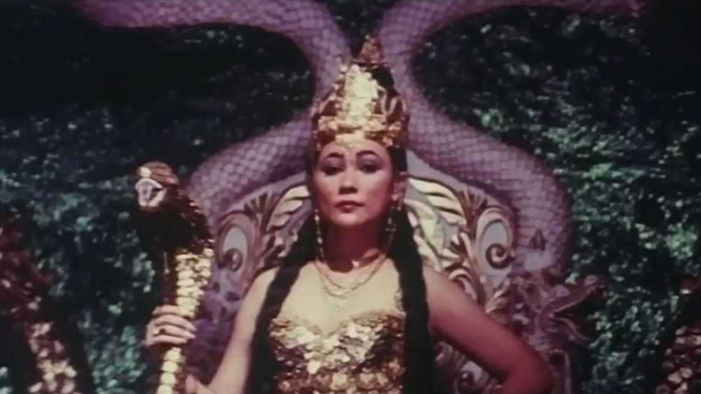 Suzzanna in NYI BLORONG (1982) in golden traditional wear, she bears a staff topped with a snake’s head.