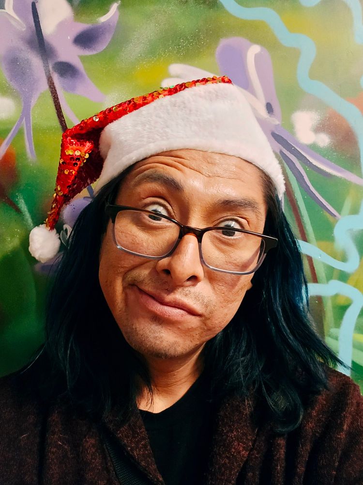 B taking a selfie at work during Christmas. Wearing red sweater, Santa had and blue hair.