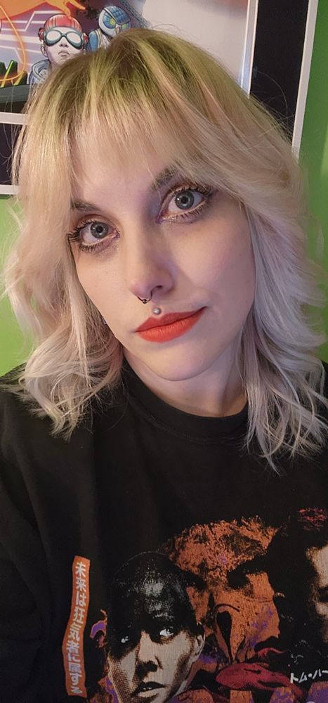 A person with light blonde hair that is half curled. They wear bright orange lipstick. 