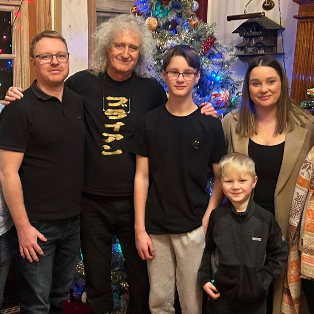 From left to right, Jacob’s dad, Sir Brian May, Jacob, his mum and younger brother, Lennon are stood smiling for a photo. Standing in a large living room with high ceilings, they’re in front of a large Christmas tree, decorated with tinsel, baubles and icy blue lights.