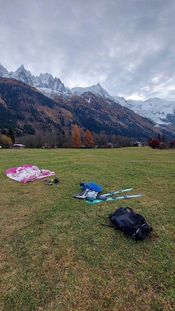 Ski de randonnée et voile de parapente posés sur l'herbe de l'atterrissage avec vue sur le mont blanc derrière