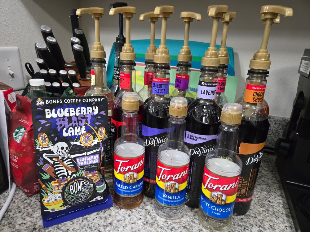 A kitchen counter with a bag of blueberries flavored coffee and various flavor syrups.
