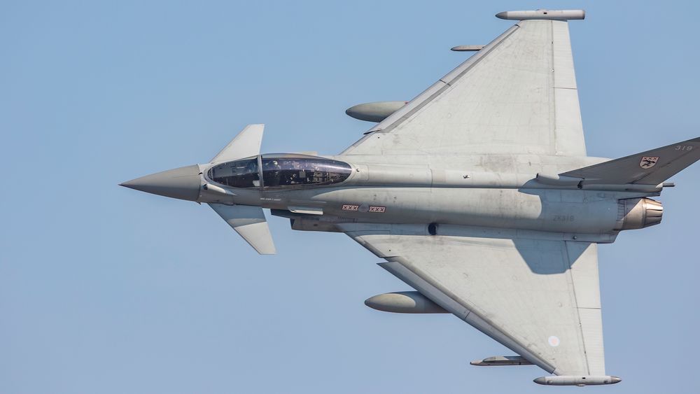Eurofighter Typhoon showing a full topside as it passes through the Mach loop, in clear blue sky.  The grey jet sports 29 squadron markings of 3 red x on a white background, surrounded in red, either side of the RAF roundel
