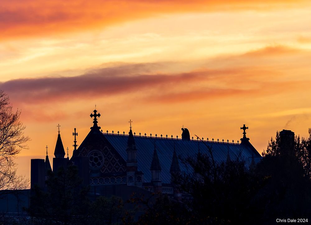 Yellow sunset over a religious building (Keble College chapel) with crosses and other roof decorations.