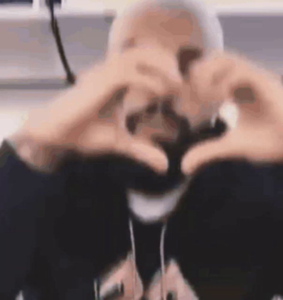 a person is making a heart shape with their hands in front of their face .