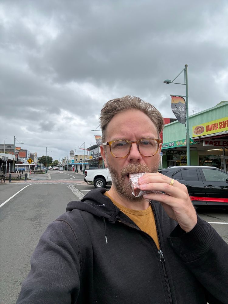 A wet man eating lolly cake on the Main Street of Hāwera. 