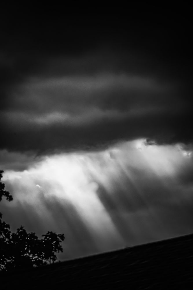 Alternating shafts of light stream from a storm cloud.  Pinhole high contrast bnw filter added in Photoshop to lend focus to the subject.  Taken yesterday evening during a severe warned storm in Coastal NJ
