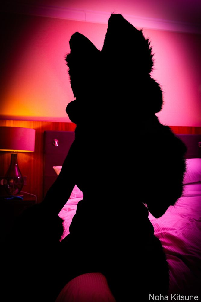 A silhouette of Cori with a bedroom background and pink lighting. 