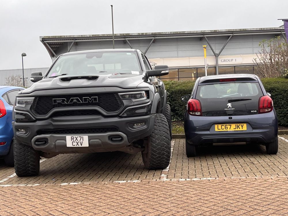 A big Dodge Ram pickup next to a small Peugeot hatchback.