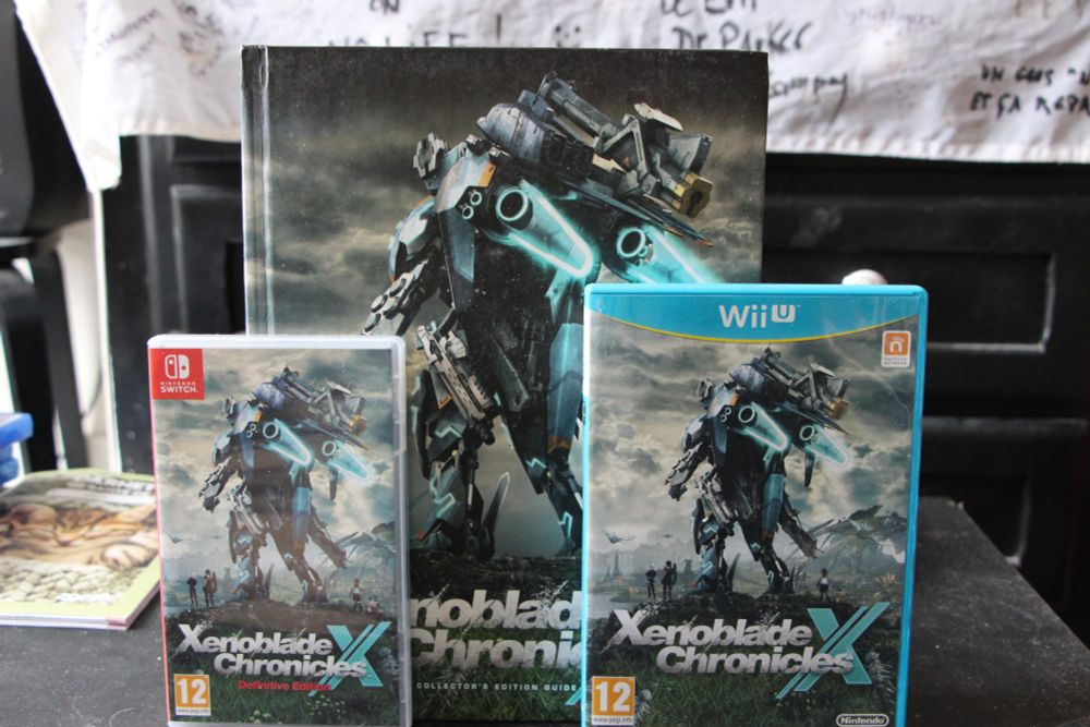 Image montrant au premier plan Xenoblade Chronicles X Definitive Edition sur Switch, Xenoblade Chronicles X  sur Wii U et le guide stratégique sorti en anglais il y a  10 ans derrière.